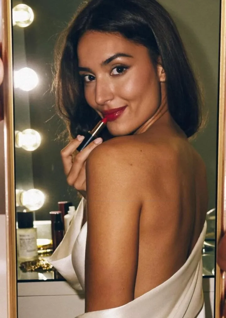 Creator at a vanity mirror applying red lipstick