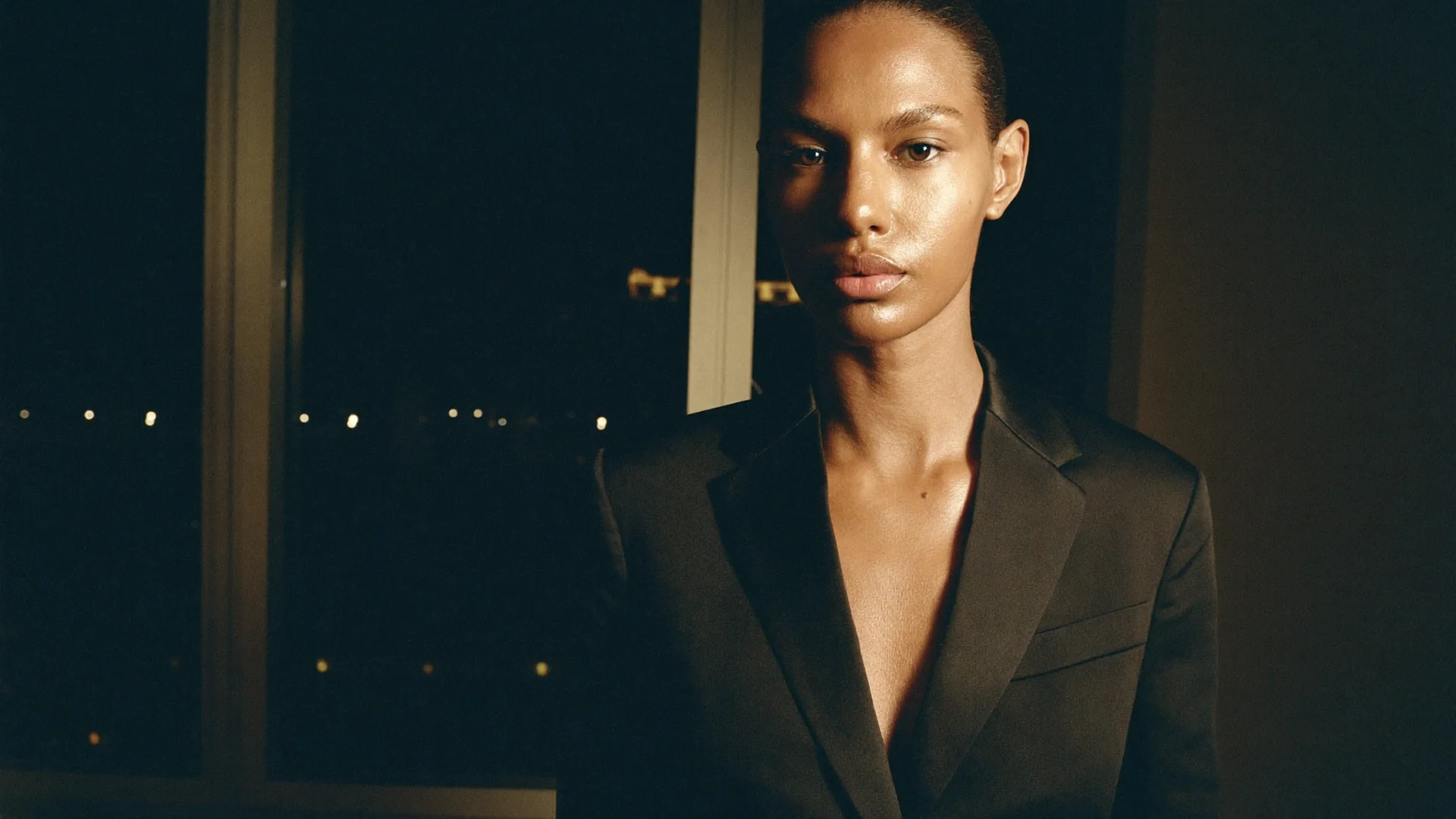 Editorial portrait of a woman in a black satin blazer in a penthouse at night